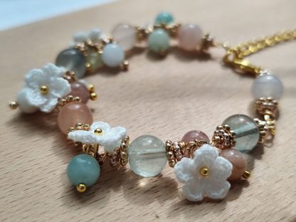 Handcrafted 'Aurelia Mist' micro crochet accessory featuring intricate, delicate patterns in soft pastel hues; an elegant, lightweight piece perfect for adding a touch of sophistication to any outfit. Displayed on a light-tone wood plate, under sunlight. The micro crochet white flowers are showing along side with the natural stone beads. The natural flourite stone beads are translucent and shining under the sunlight.