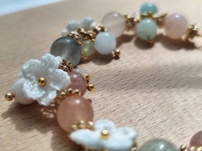 Handcrafted 'Aurelia Mist' micro crochet accessory featuring intricate, delicate patterns in soft pastel hues; an elegant, lightweight piece perfect for adding a touch of sophistication to any outfit. Displayed on a light-tone wood plate, under sunlight. The micro crochet white flowers are showing along side with the natural stone beads. The natural flourite stone beads are translucent and shining under the sunlight.