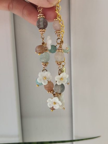 Handcrafted 'Aurelia Mist' micro crochet accessory featuring intricate, delicate patterns in soft pastel hues; an elegant, lightweight piece perfect for adding a touch of sophistication to any outfit. Displayed on a light-tone wood plate, under sunlight. The micro crochet white flowers are showing along side with the natural stone beads. The natural flourite stone beads are translucent and shining under the sunlight.