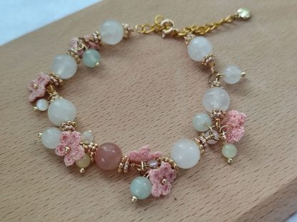 the white quartz crystal bracelet with pink micro crochet flowers，with gold tone chain laid flat on a light tone wood board