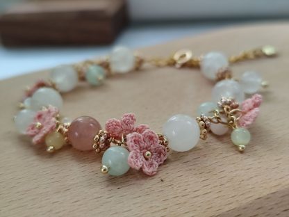 the white quartz crystal bracelet with pink micro crochet flowers，with gold tone chain laid flat on a light tone wood board