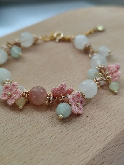 the white quartz crystal bracelet with pink micro crochet flowers，with gold tone chain laid flat on a light tone wood board